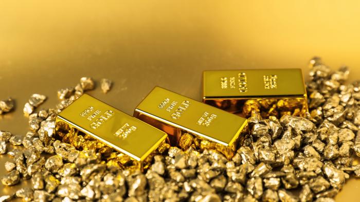Goldnuggets und Goldbarren auf glänzendem Hintergrund, Nahaufnahme
